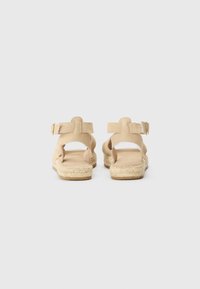 Beige nubukist sandaalid espadrillide tallaga. Omavad reguleeritavaid pahkluu rihmasid, avatud kannaosa ja tekstureeritud jute ümbrist tallal.