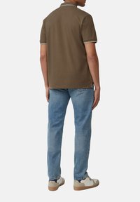 Braunes Poloshirt mit weißen Akzenten, getragen mit leicht verwaschenen blauen Jeans und beigen Sneakern. Lässige und figurbetonte Silhouette.