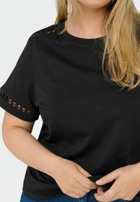 Camiseta negra de manga corta hecha de algodón, con detalles de encaje en los brazos, escote redondo y un corte holgado.