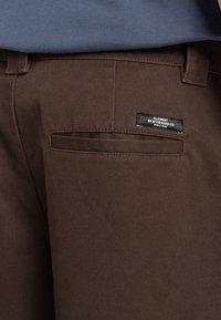 Brown cotton skate pants with a back pocket featuring a black Element Skateboard Co. label, showcasing a textured, durable fabric.