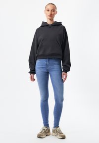 Mörkgrå kort hoodie med en framficka, kombinerad med ljusblå skinny jeans och beige sneakers med grå accenter.
