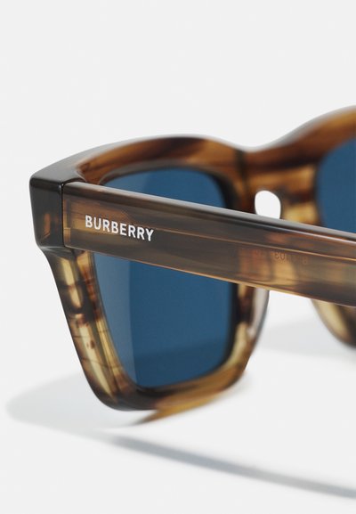 Burberry napszemüveg barna teknősbékahatású kerettel és kék lencsékkel. Jellemzői közé tartozik a merész formák, a textúrázott karok és a fehér márkaneves részlet.