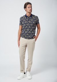 Marineblauw bloemmotief polo met een contrasterende kraag, gecombineerd met lichtbeige broek en witte sneakers. Beschikt over een getailleerd ontwerp en korte mouwen.