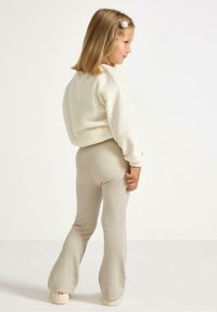 Sweter polarowy w kolorze off-white i prążkowane legginsy w odcieniu beżu. Legginsy mają rozszerzający się dół i miękką strukturę.
