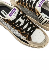 Sneakers in pelle con stampa animale, dettagli in glitter argento e lacci neri. La punta è bianca con piccole perforazioni.