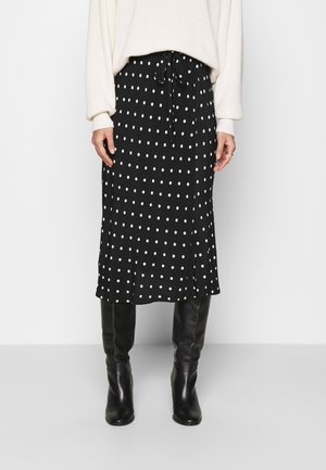 Black midi skirt with white polka dots, drawstring waist, and slight side slit, paired with black knee-high boots. Soft fabric and relaxed fit.