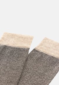 Stickade strumpor med en beige toppkant och en gradientdesign som övergår till en mörkgrå nederdel, med en jämn textur.