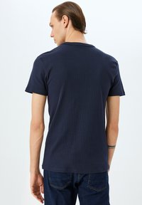 Marineblå ribbet T-shirt med korte ærmer, der har en rund halsudskæring og en tekstureret overflade, parret med mørke jeans.