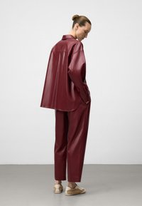 Burgunderfarbene Kunstleder-Übergrößenshirt und passende Hose; matte Oberfläche; lockere Passform; das Shirt verfügt über einen Kragen und eine Rückenpasse.