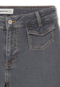 Jeans de mezclilla gris con costuras naranjas, cierre frontal con botón y un pequeño bolsillo trasero. La tela tiene un acabado suave, ligeramente texturizado.