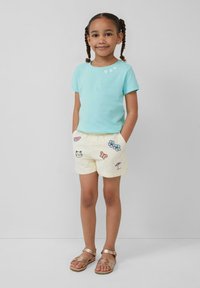 Lichtblauw katoenen T-shirt met drie kleine witte hartversieringen. Crème shorts met diverse kleurrijke geborduurde ontwerpen en een elastische tailleband.