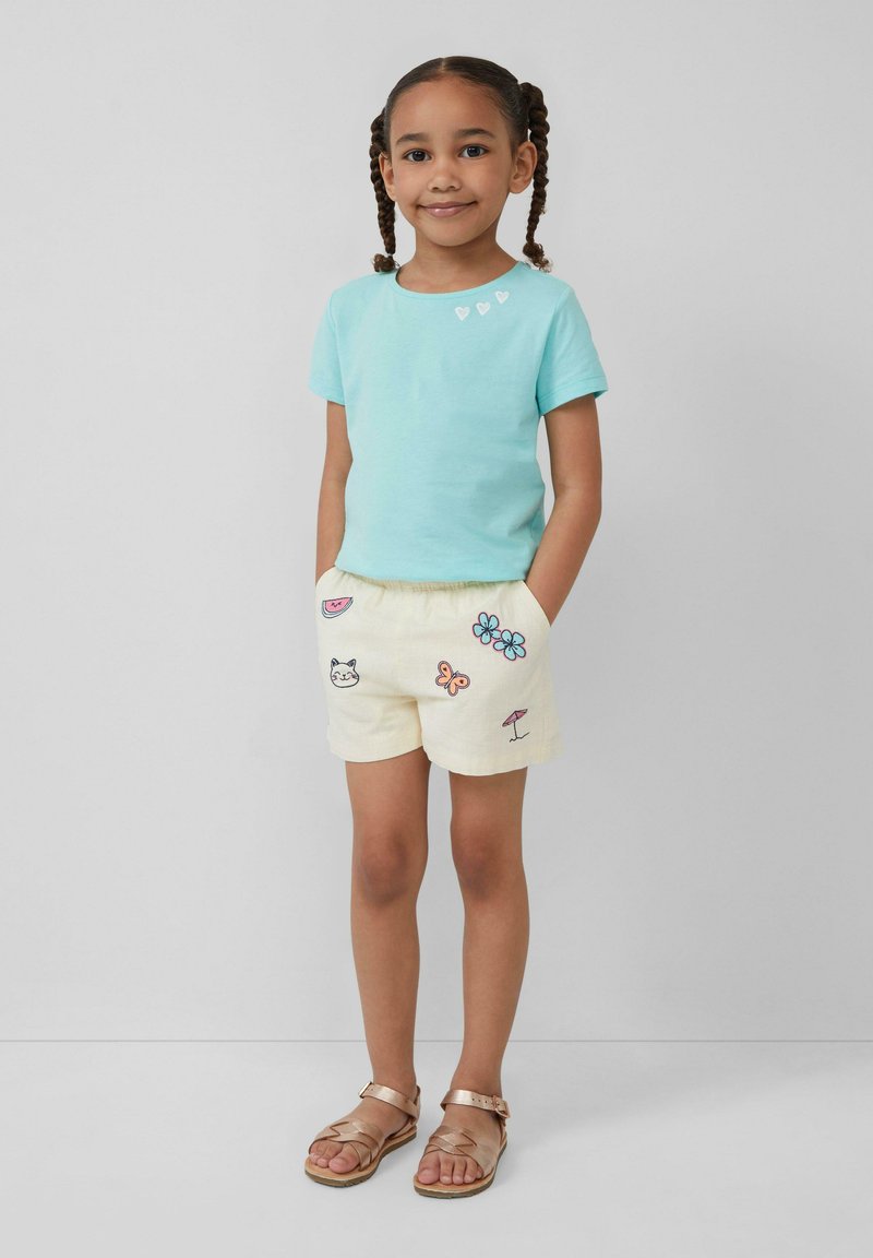 Lichtblauw katoenen T-shirt met drie kleine witte hartversieringen. Crème shorts met diverse kleurrijke geborduurde ontwerpen en een elastische tailleband.