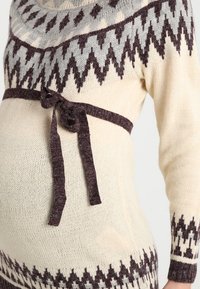 Sweter dziany w kremowym kolorze z szarymi i ciemnobrązowymi wzorami w zygzak, z dopasowanym, wiązanym paskiem w talii oraz długimi rękawami.