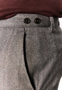 Szare spodnie o wzorze jodełki z teksturowanej tkaniny, z dwoma ciemnymi guzikami w pasie i plisowanym przodem.