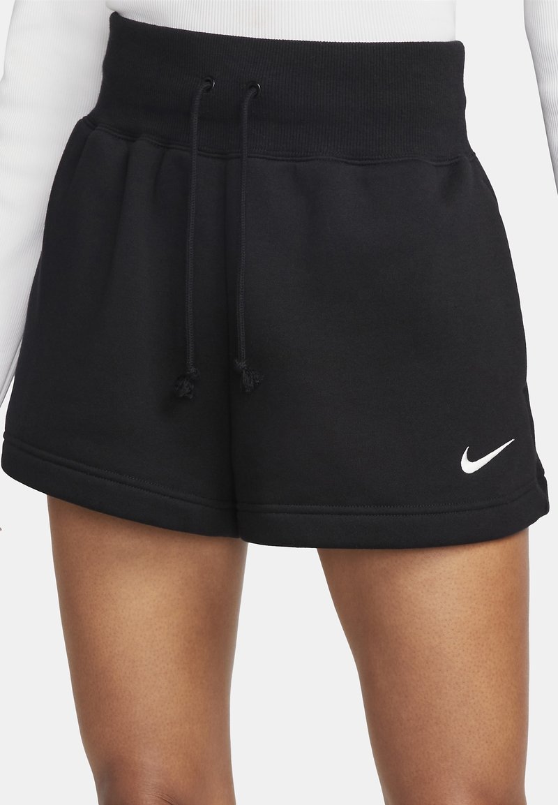 Shorts de sport noirs avec une large taille côtelée et un cordon, petit logo blanc Nike sur l'ourlet gauche, portés sur des jambes nues.