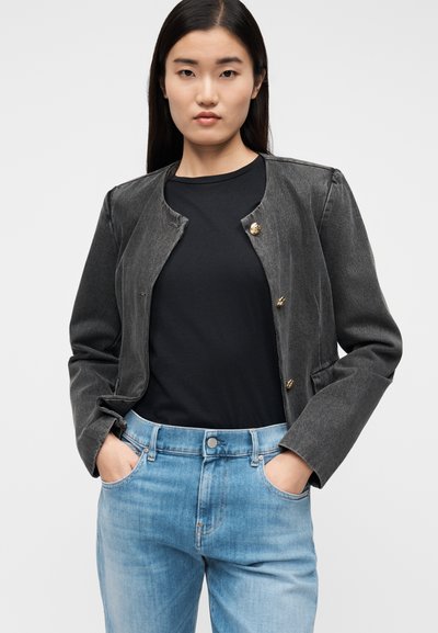 Svart jeansjacka med rund halsringning och gyllene knappar, kombinerad med en svart skjorta och ljusblå jeans. Mjuk textur.