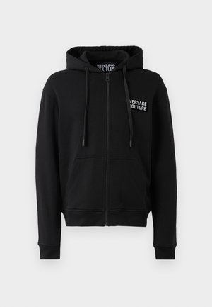 Črna zip-up kapuca s kapuco na vrvico, ki ima sprednji žep in belo Versace Jeans Couture logotip na levem prsnem delu. Mehak teksturiran material.