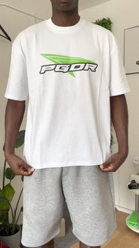 Hvid t-shirt med korte ærmer og et grønt og sort "PGDR" logo, lavet af glat stof, båret over grå shorts.