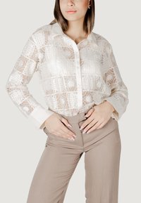 Valge pitsbluus, millel on kaelus ja nööpidega esiosa, millel on keerukad mustrid. Koos kergelt beežide kõrge vöökohaga pükstega.