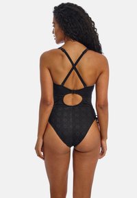 Sort énstykket swimsuit med tekstureret stof, krydsede skulderstropper og et cirkulært udskæringsdetalje på ryggen.