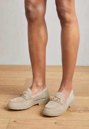 Beige ruskind loafers med guldkædehardware og en tekstureret sål, som har en lav profil og et rundt tådesign.