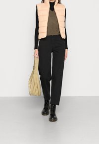 Jasnoróżowa pikowana kamizelka na ciemnym swetrze, zestawiona z czarnymi spodniami z wysokim stanem i czarnymi wiązanymi butami. Całość dopełnia beżowa torebka.