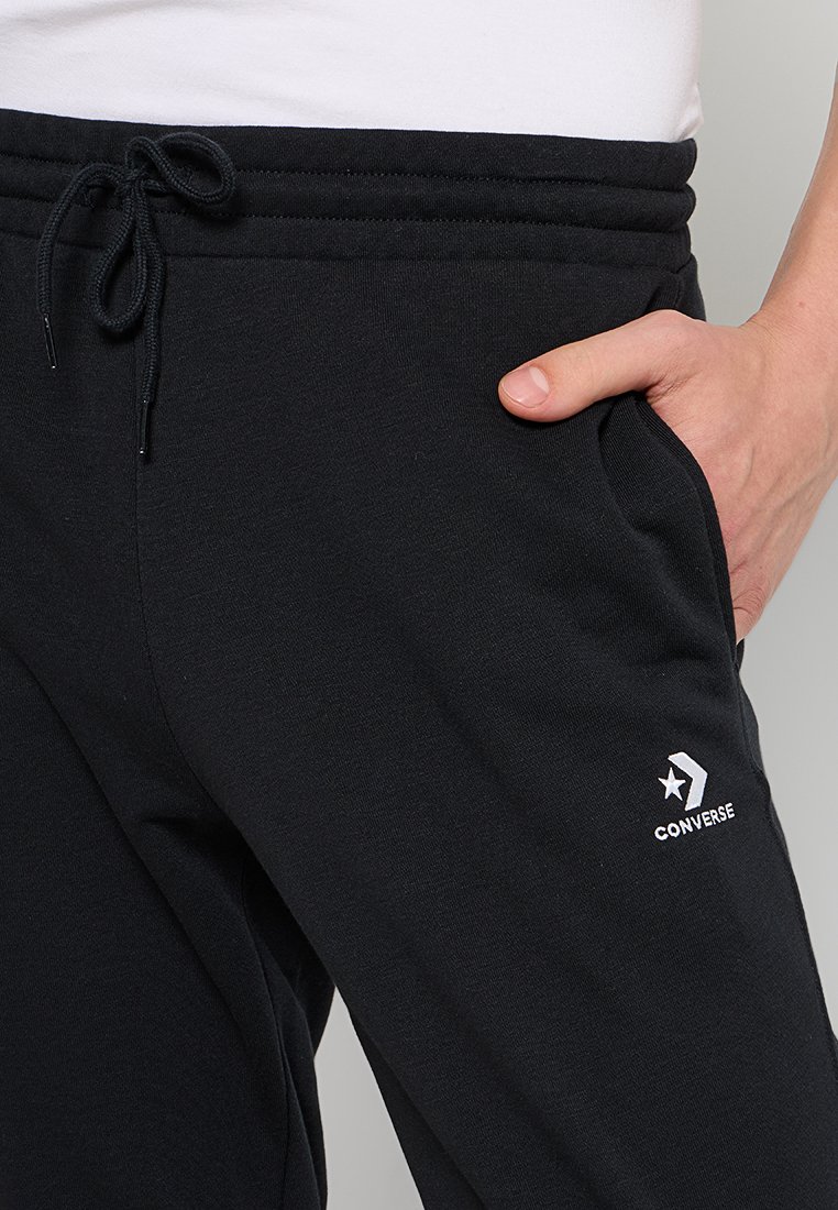 Jogging neri in cotone con cintura regolabile, tasche laterali e logo bianco Converse vicino alla tasca destra. Texture liscia.