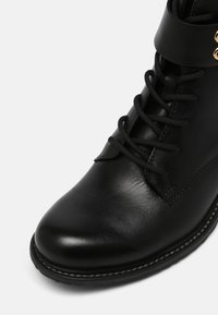 Botte noire en cuir à lacets, avec bout arrondi, couture le long de la semelle, et œillets dorés près du haut.