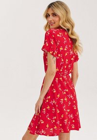 Czerwona sukienka w kwiaty z krótkimi falbaniastymi rękawami, ozdobiona żółtymi i różowymi kwiatami. Miękka, lekka tkanina z falującym fasonem spódnicy.