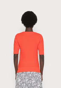 Top aderente arancione a maniche corte in maglia, con un motivo texturizzato e orlo a costine, abbinato a una gonna floreale in bianco e nero.