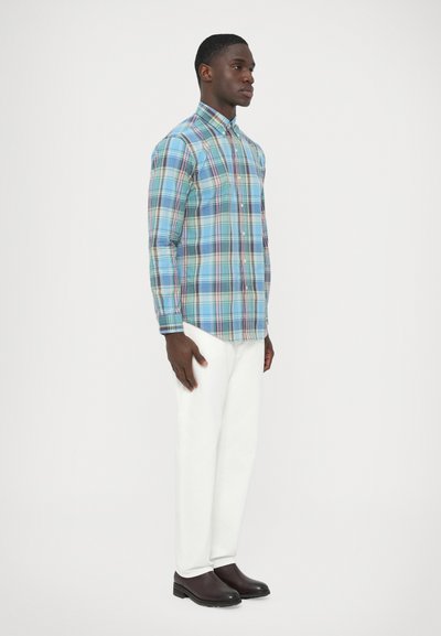 Svetlo modra karirana srajca z gumbi, ki jo krasijo zelene, bele in sive črte, kombinirana z belimi hlačami in rjavimi čevlji. Gladek bombažen material.