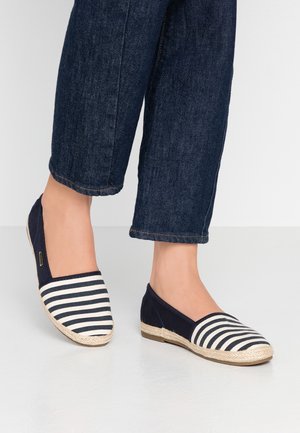 Alpargatas a rayas con lona azul marino y rayas blancas, con suela trenzada de yute. Llevadas con vaqueros oscuros recortados.