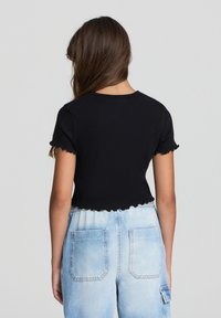 Czarny krótki top z krótkimi, falbaniastymi rękawami i teksturowanym, prążkowanym wzorem, w połączeniu z jasnoniebieskimi, wysokimi dżinsami z tylnymi kieszeniami.