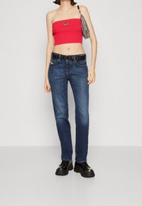 Röd ribbad kort topp, blå denimjeans, svart nitarbälte, svarta platåskor, silverväska, inomhusmiljö, neutral bakgrund.