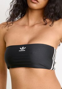 Top de bikini preto sem alças, feito de um tecido macio e elástico, com um logo branco da Adidas e riscas brancas nas laterais.