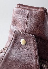 Brown leather backpack featuring a textured surface, bronze hardware, and a top flap with visible stitching and zipper detail.
