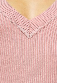 Rosa ribbad stickad topp med V-ringning, texturerad yta och vertikala ränder, som visar upp ett mjukt och lätt tyg.