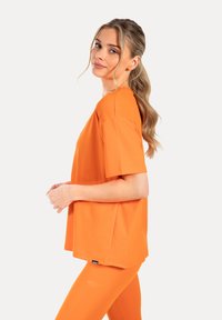 Oranje atletisch shirt met korte mouwen, gemaakt van gladde stof, met een losse pasvorm en ronde hals, gecombineerd met bijpassende oranje leggings.