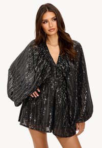 Robe en sequins noirs avec un décolleté en V profond, des manches bouffantes surdimensionnées et une taille froncée. Présente un motif texturé et chatoyant sur l'ensemble.