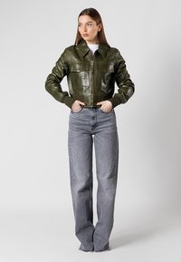 Veste en cuir vert raccourcie avec deux poches avant, fermeture éclair et poignets côtelés, associée à un jean en denim gris taille haute.
