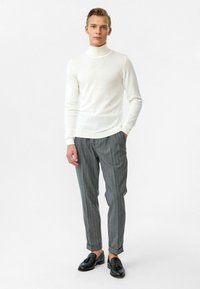 Witte coltrui, lichtgewicht breiwerk, gecombineerd met grijze broek met streepjes, omgeslagen bij de enkel, afgewerkt met zwarte instappers.