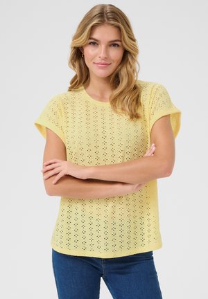 Yellow short-sleeve top featuring an eyelet pattern with diamond shapes. The shirt has a round neckline and a relaxed fit.