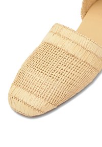 Mule tissée beige à bout fermé avec une texture complexe semblable à de la paille et une semelle plate, vue en gros plan d'un angle supérieur.