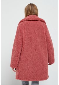 Przewymiarowany, różowy płaszcz typu teddy wykonany z miękkiego, puszystego materiału. Posiada szeroki kołnierz i opadające ramiona, o prostym kroju.