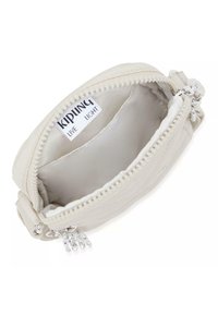 Krämfärgad tygpung med dragkedja, med ett mjukt foder och en metallberlock som accent. Inuti finns en etikett med texten "KIPLING LIVE LIGHT."