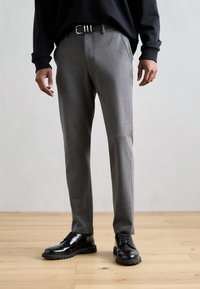 Sivo krojene hlače z gladkim zaključkom tkanine, združene s črnimi usnjenimi čevlji z debelim podplatom in vezalkami.