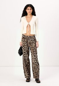 Kremasti pleteni top s rebrastim uzorkom i vezanjem, u kombinaciji sa širokim hlačama s leopard uzorkom. Model drži crnu torbu i nosi smeđe platforme čizme.