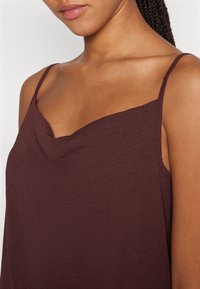 Burgundy spetstopp med djup V-ringning, tunna justerbara axelband och en texturerad tygkvalitet för ett mjukt utseende.