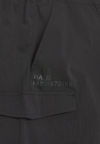 Czarna tkanina z patką na kieszeń i skośną boczną kieszenią, z nadrukowanym tekstem "HALO" oraz cyframi "198819721981" blisko kieszeni.