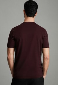 Tricou scurt, de culoare maroon, cu guler rotund, fabricat din material moale. Textură netedă, cu o siluetă ajustată, văzut din spate.